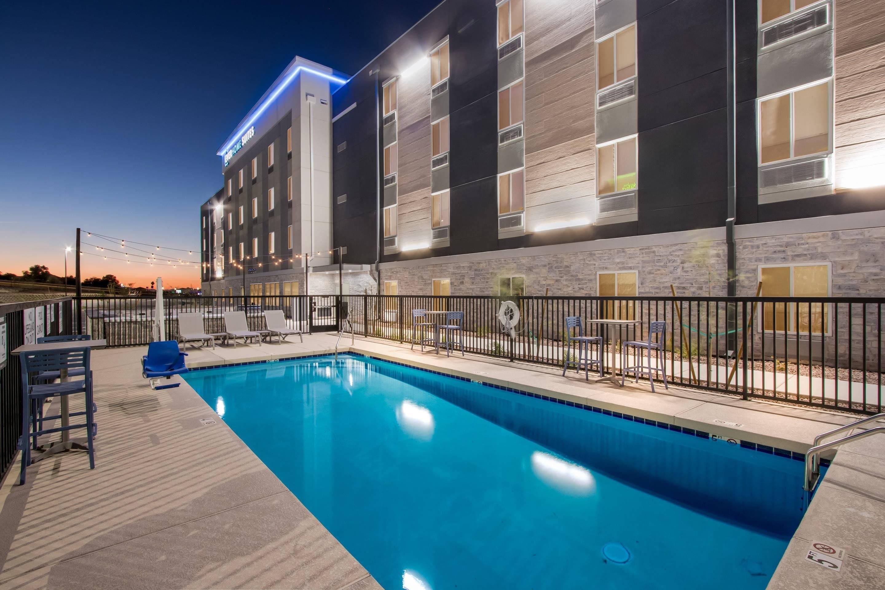 A modern hotel with a swimming pool, outdoor seating, and a well-lit facade.