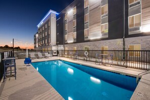Un hôtel moderne doté d’une piscine, d’un espace extérieur aménagé et d’une façade bien éclairée.