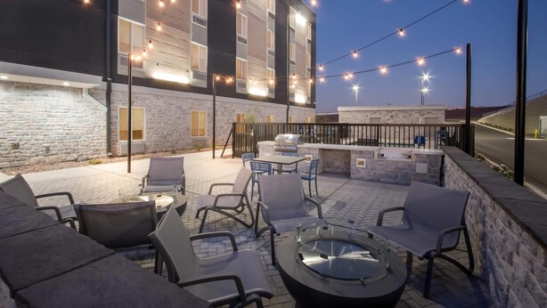 Een terras buiten met zitplaatsen, een barbecuehoek en lichtjes langs het gevelfront.