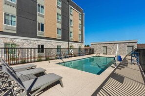 Un hôtel moderne doté d’une piscine, de chaises longues et d’une façade en pierre.