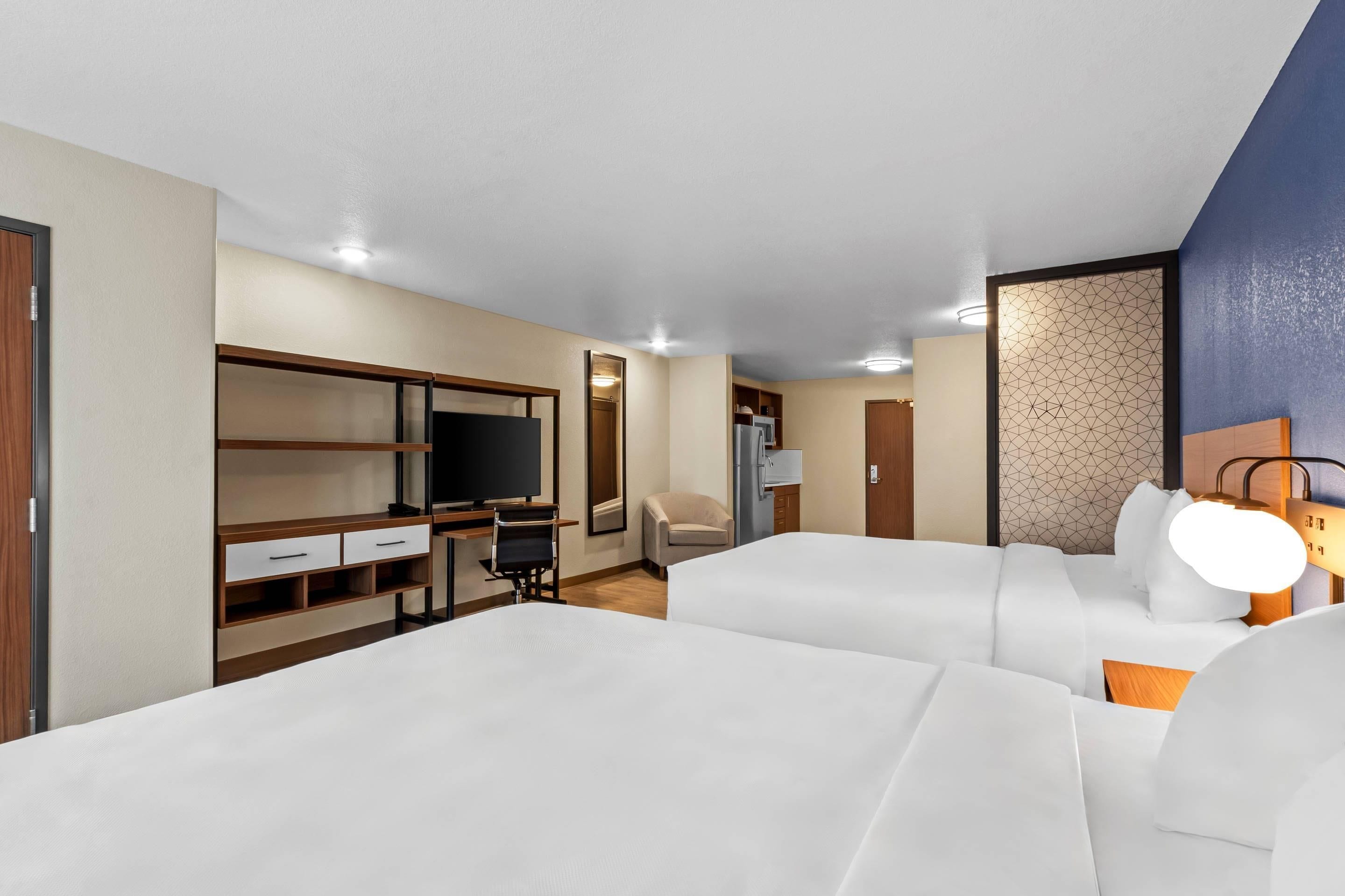 Een hotelkamer met twee bedden, een bureau met stoel, een televisie en een kledingkast.