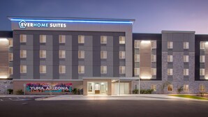 Een modern hotelgebouw met het bord 'Everhome Suites' en een muurschildering van het landschap van Yuma, Arizona.