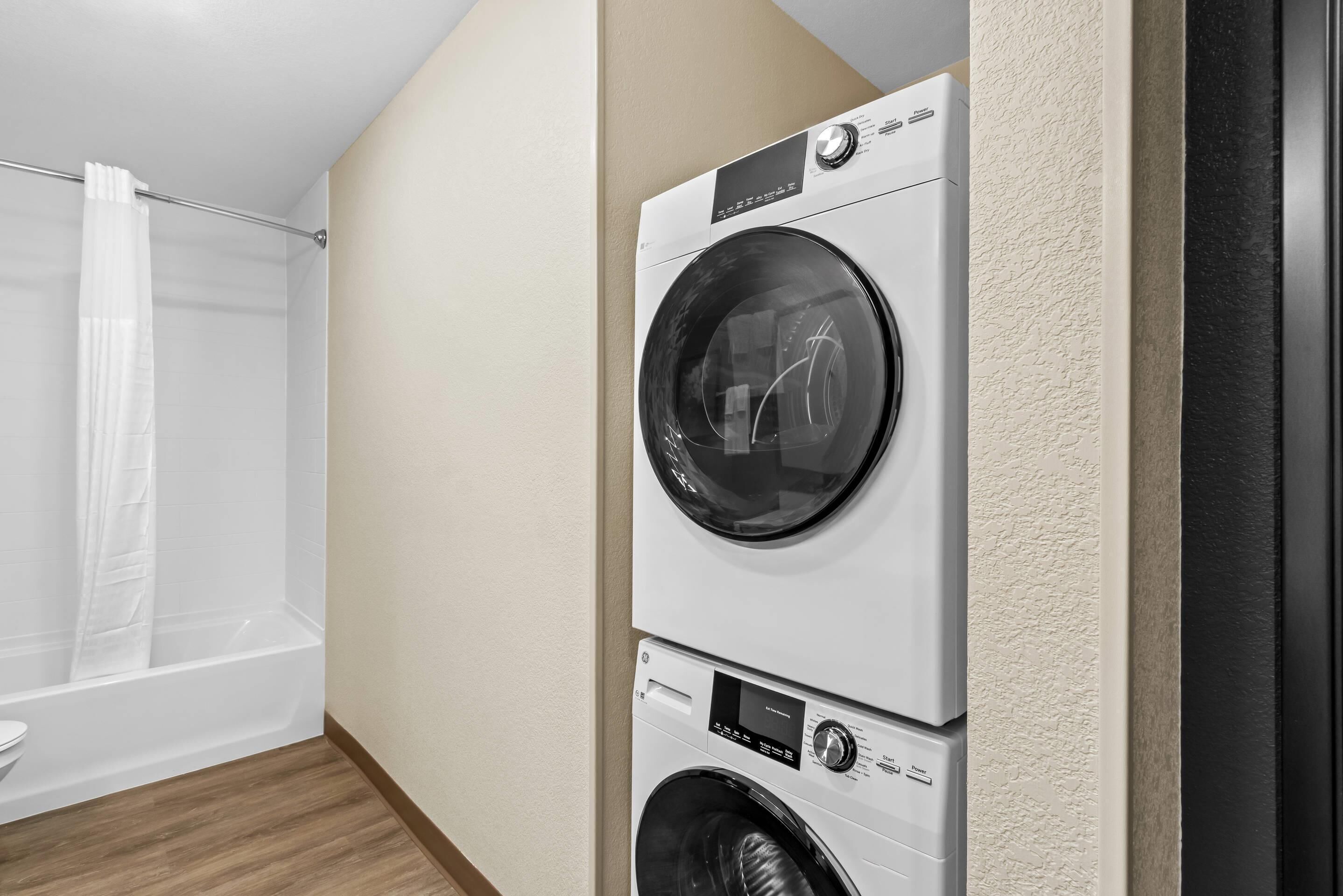 A laundry room with two stacked front-loading washing machines and a shower area with a white curtain.