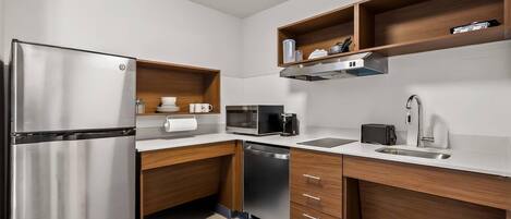 A compact kitchen with a stainless steel refrigerator, a microwave, a dishwasher, wooden cabinets, and a countertop with a sink and a toaster.