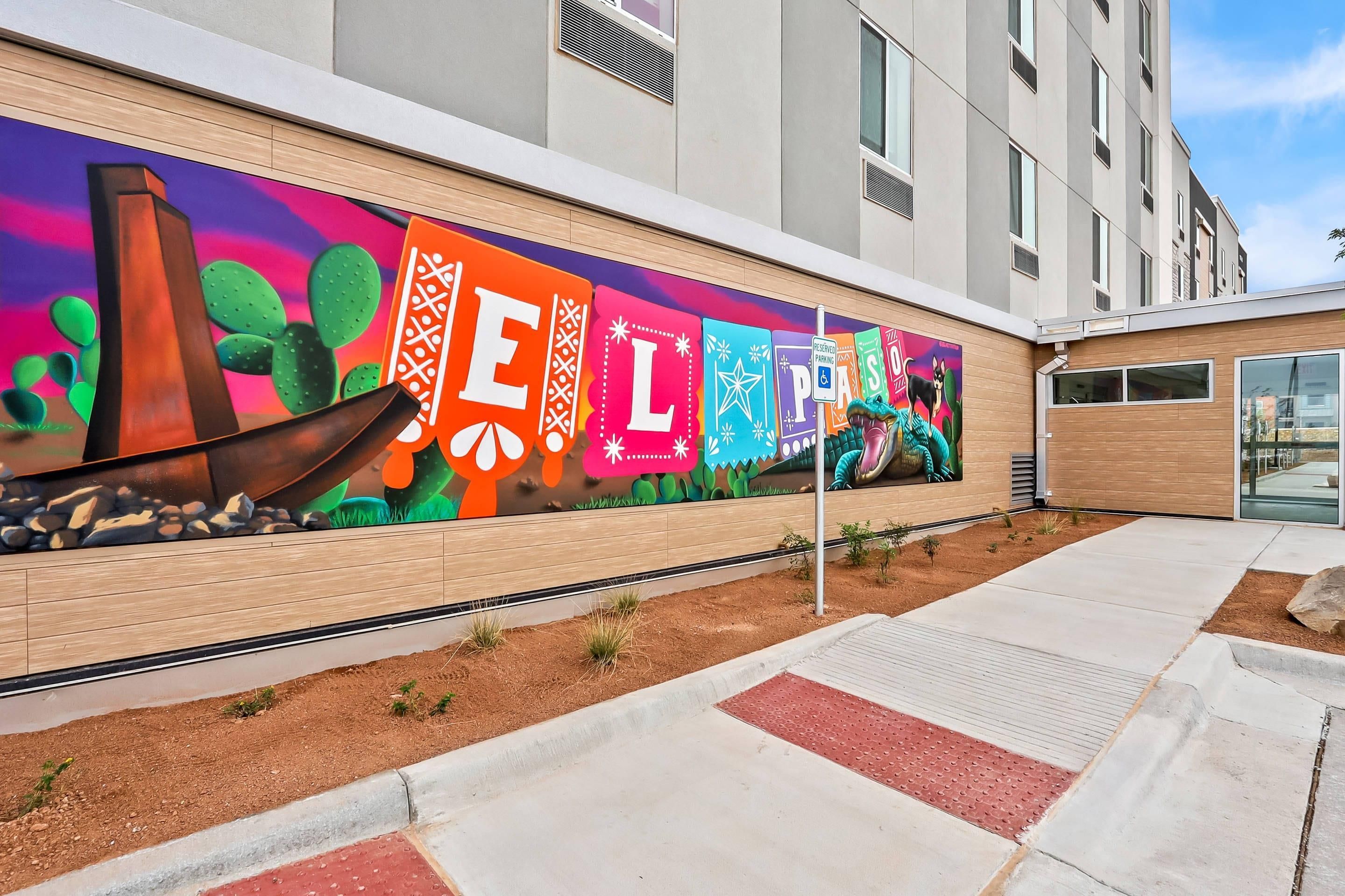 Exterior d'un edifici amb un mural de colors que representa lletres i cactus.