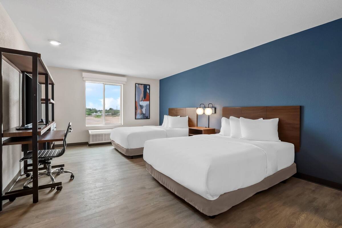 A hotel room with two beds, a desk, and a chair.