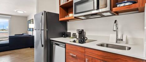 Una cocina moderna con refrigerador, microondas y cafetera. Hay un gabinete de madera sobre el fregadero y un lavavajillas a la izquierda.
