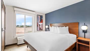 Une chambre d’hôtel moderne dotée d’un grand lit, offrant une vue sur l’extérieur, d’une œuvre d’art accrochée au mur et d’une table de chevet avec une lampe.
