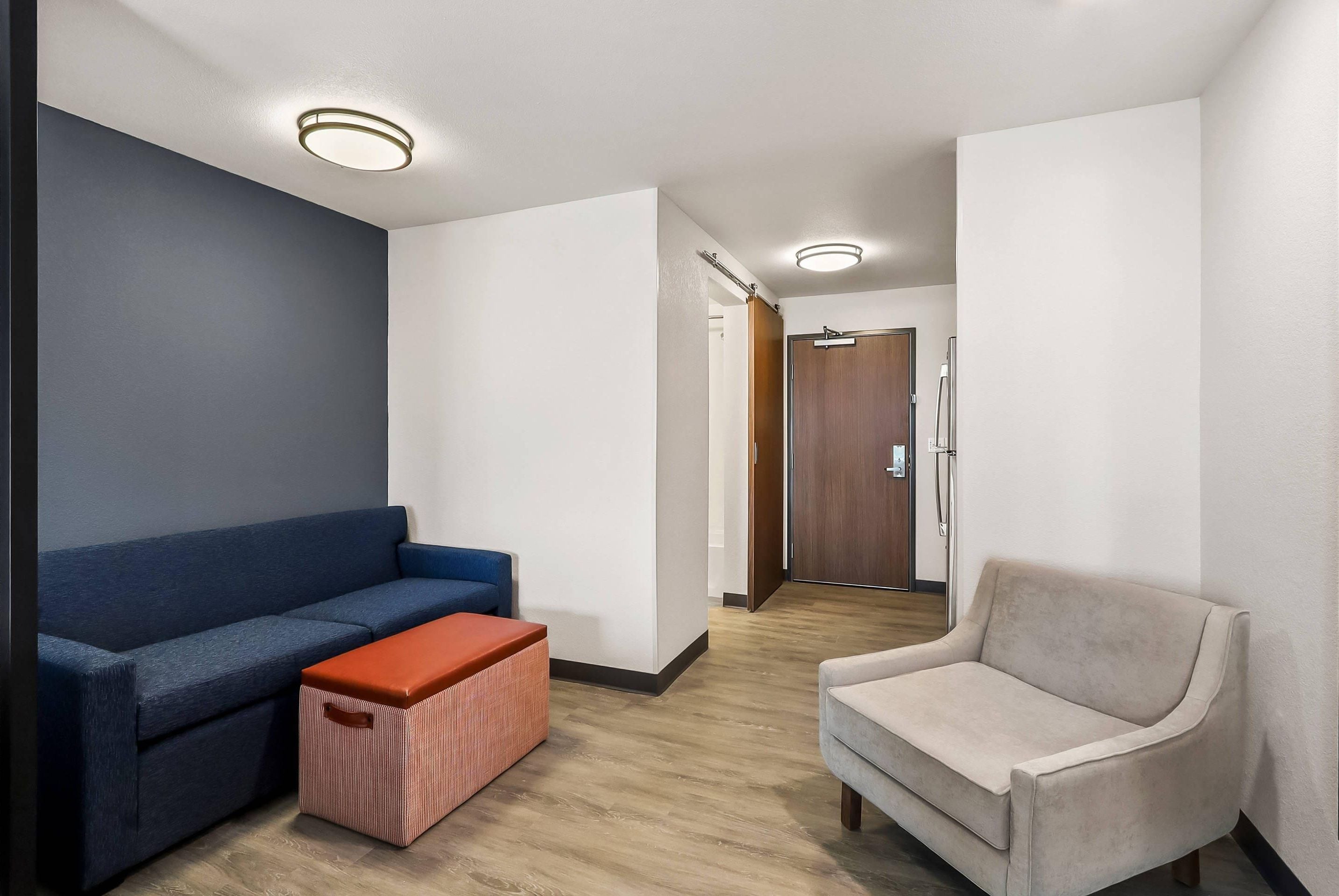 Un salon moderne avec un canapé bleu, un fauteuil beige et un plancher en bois.