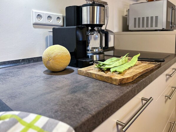 Un plan de travail de cuisine avec un melon, des haricots verts et une machine à café.