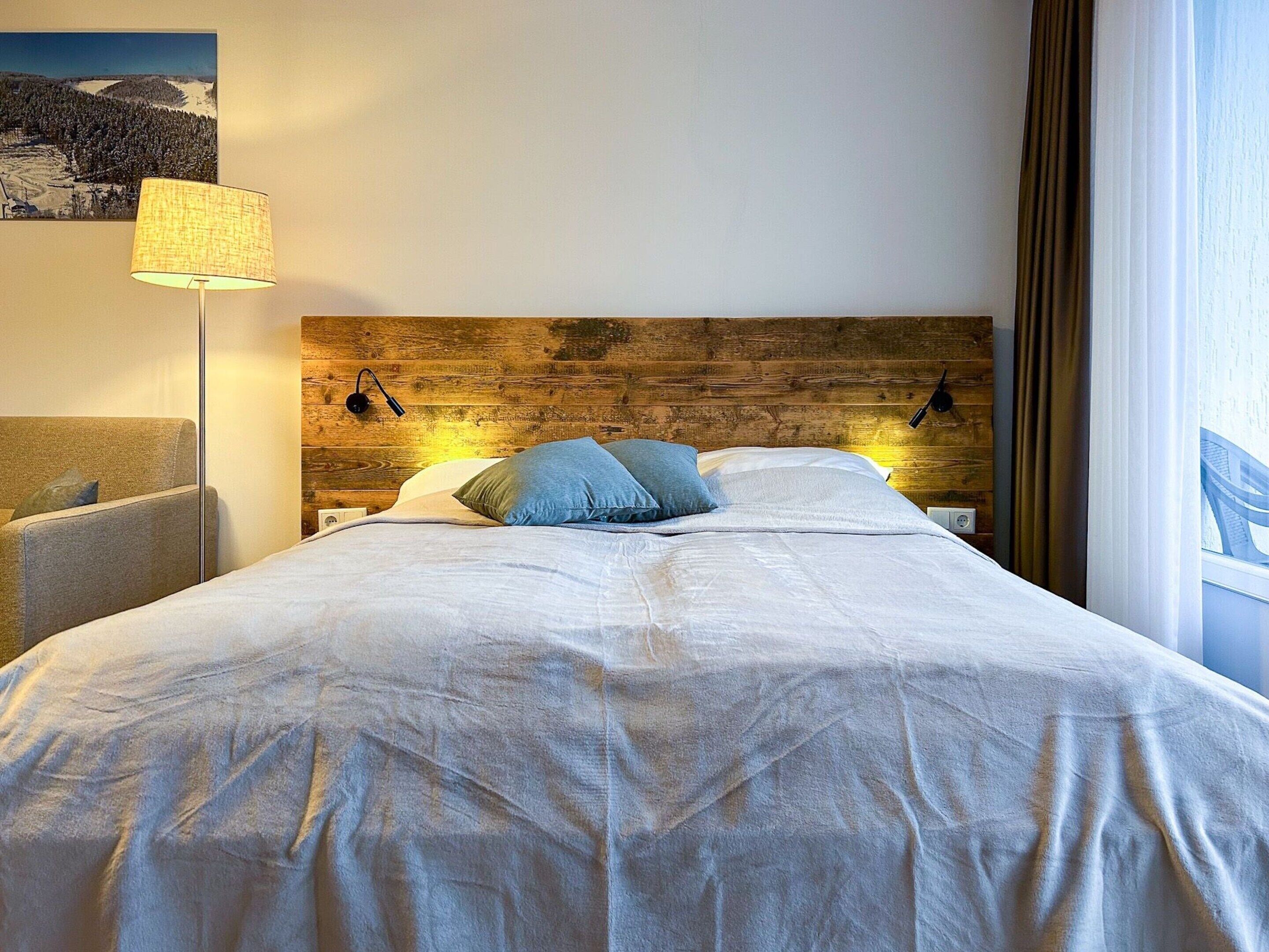 A neatly made bed with a wooden headboard, two bedside lamps, and a single pillow.