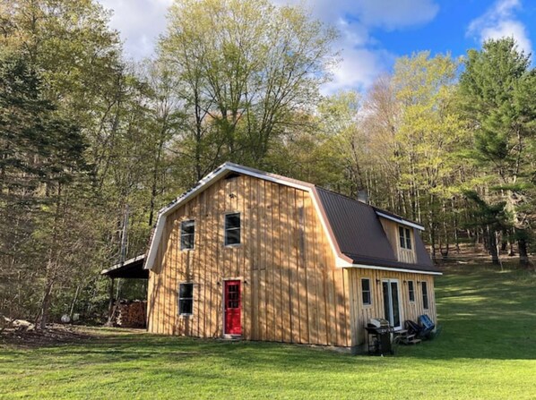 Situated in a lush landscape, this rustic barn-style building features a prominent red door and a sloped roof.