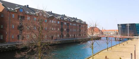 A riverside walkway with a brick building and a modern structure in the background.
