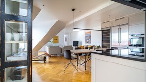 A modern kitchen with white cabinets, a large island, and a dining area with a table and chairs. - Heart of the city Penthouse with rooftop terrace (København)