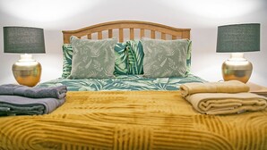 A bed with a wooden headboard, two bedside lamps, and a green patterned bedspread. - Castle Street Apartments | Grampian Lettings Ltd (Aberdeen)