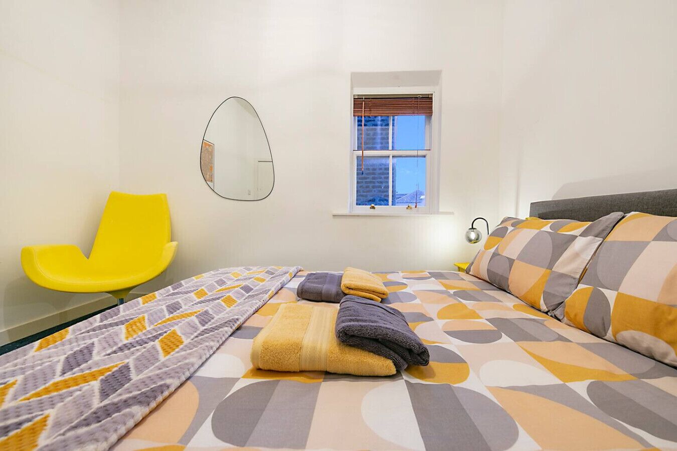 Une chambre à coucher avec un lit, une chaise, une fenêtre et un miroir.