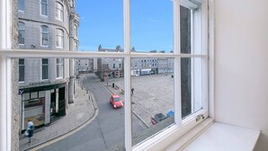 A street view through a window with buildings, a clear sky, and a red car on the road. - Castle Street Apartments | Grampian Lettings Ltd (Aberdeen)