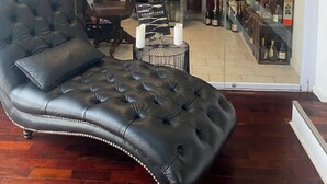 A room with a leather sofa, a glass door leading to a wine cellar, and wooden beams on the ceiling.