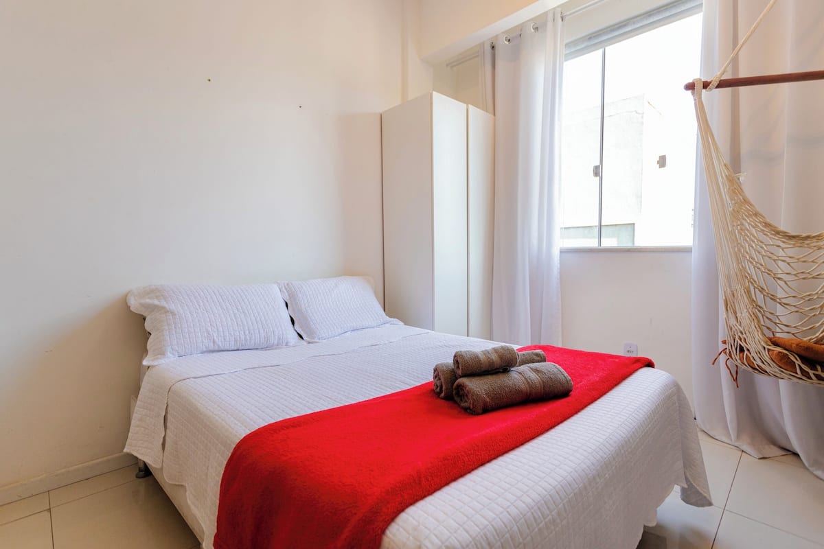 Une chambre d’hôtel avec un lit, une couverture rouge et un hamac.