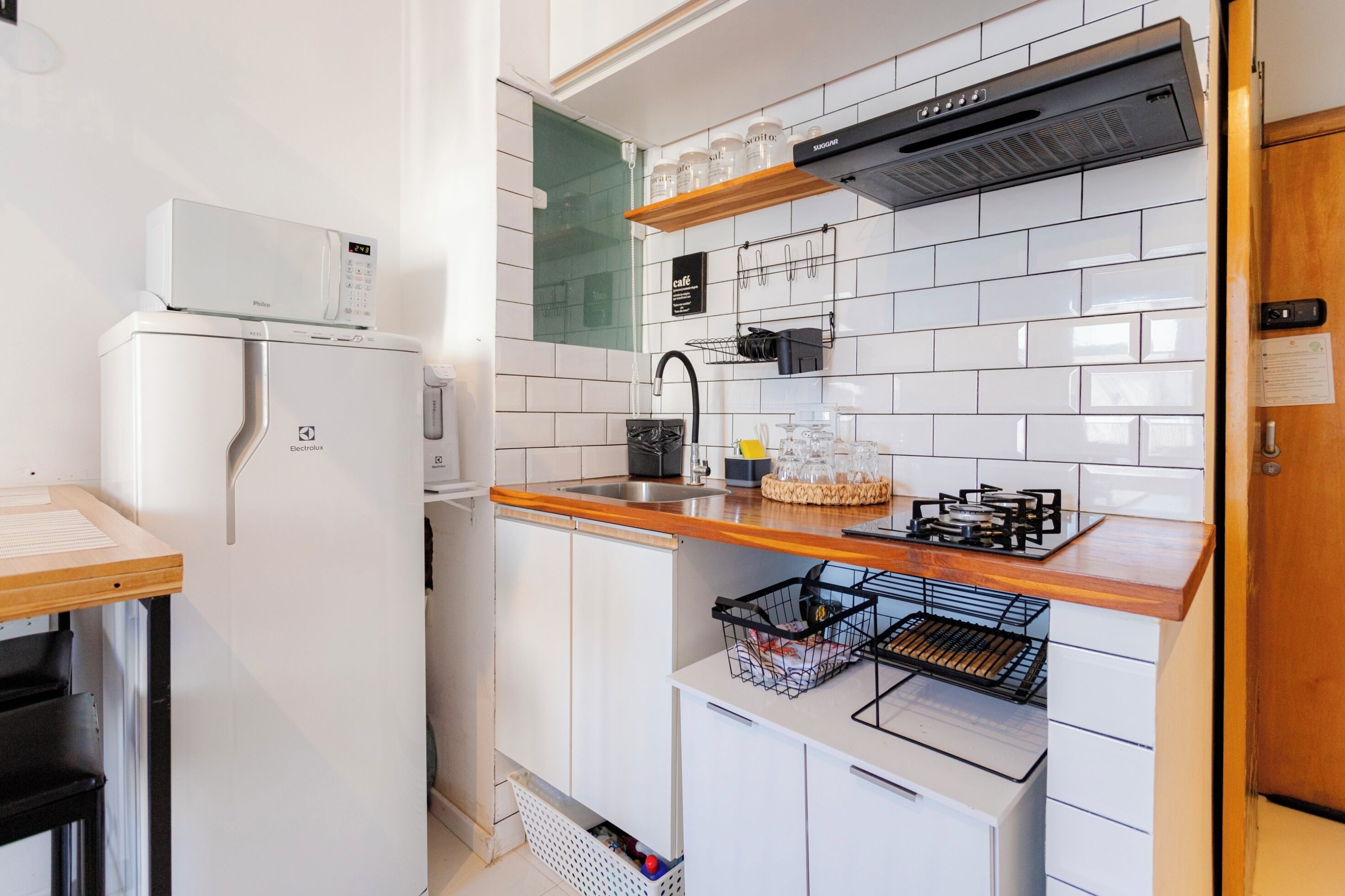 Una cocina compacta con armarios blancos, un microondas, una cafetera, un lavamanos y una encimera de madera.