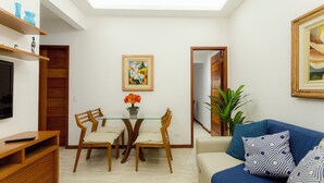 Un coin repas avec une table en verre et des chaises en bois, un canapé agrémenté de coussins à motifs et un tableau accroché au mur.