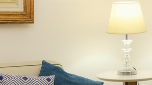 Un canapé beige agrémenté d’un plaid bleu et de deux coussins : l’un présente un motif géométrique, l’autre est d’un bleu uni. Une lampe de table blanche, avec un abat-jour transparent, est posée sur une petite table en bois, à côté du canapé.