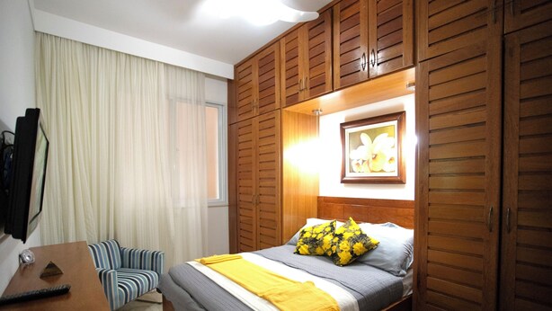 Une chambre à coucher avec un lit, une table de chevet, une chaise, une armoire et un cadre photo accroché au mur.