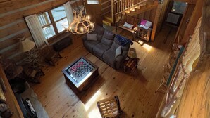 Ein geräumiger Loft-Raum mit hohen Decken, Holzbalken, einer gemütlichen Sitzecke mit Sofa und Couchtisch sowie einer Treppe, die zu einer erhöhten Ebene führt.