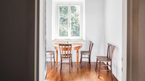 A dining area with a round table and four chairs, a window with a view of greenery, and a hanging light fixture. - DADI INN MONTI (Rome)