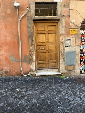 A wooden door with a metal handle, a small step leading up to it, and a utility box to the left. - DADI INN MONTI (Rome)