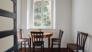 A dining area with a round wooden table, four wooden chairs, and a window with a view of trees. - DADI INN MONTI (Rome)