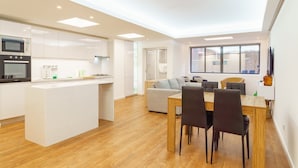 Una cocina moderna con una isla central, un comedor con mesa y sillas de madera, y una sala de estar con sofá y sillones.