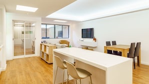 Una cocina moderna con una isla central, un comedor con mesa y sillas de madera, y un ventanal que proporciona luz natural.