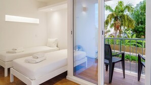 Una habitación con dos camas, una puerta corrediza de vidrio a un balcón y una silla afuera.