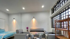 A modern living room with a sofa set, a coffee table, and a bed with a blue headboard. - Cassiarata (Phnom Penh)