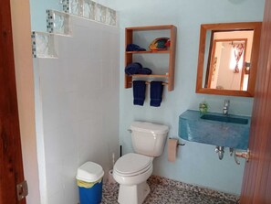 A bathroom with a toilet, a sink, and a shelf with towels.