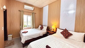 A hotel room with two beds, a window with curtains, an air conditioning unit, and a nightstand with a lamp. - The Palm Lodge (Phong Nha)