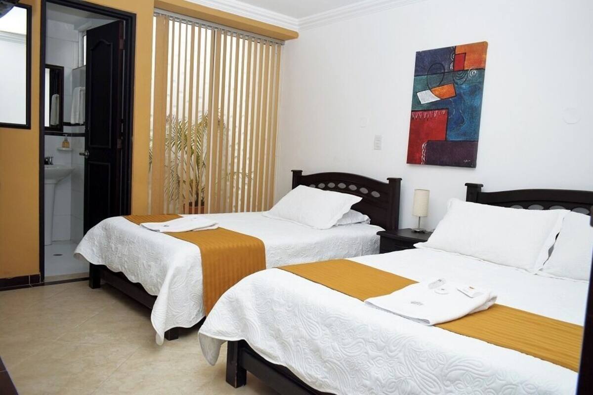 A hotel room with two beds, a bathroom, and a painting on the wall.