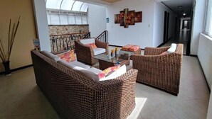 A spacious living area with wicker furniture, a glass coffee table, and a view of a stone wall and staircase. - HOTEL SAN JERONIMO POPAYAN (Popayán)