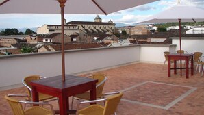 A terrace with a table and chairs, a large umbrella, and a view of historic buildings. - HOTEL SAN JERONIMO POPAYAN (Popayán)