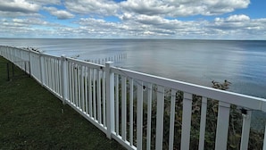 A white fence overlooking a calm body of water with a clear sky.