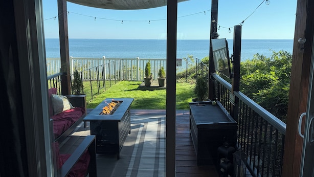 A balcony with a view of the sea, a fire pit, outdoor furniture, and string lights.