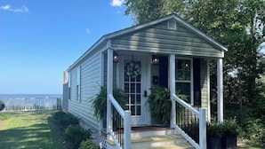 A small, single-story house with a porch, white railings, and a view of the ocean.