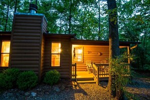 Eine Blockhütte mit Schornstein, einer Veranda mit Bank und einem kleinen Garten.