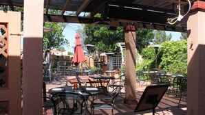 Une terrasse extérieure avec des tables et des chaises, un parasol rouge et une structure en forme de pergola.