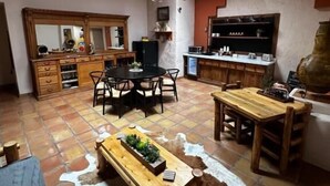 Un vaste espace de vie doté d’un haut plafond, de poutres apparentes, d’une grande table à manger et d’un coin cuisine équipé d’appareils électroménagers modernes.