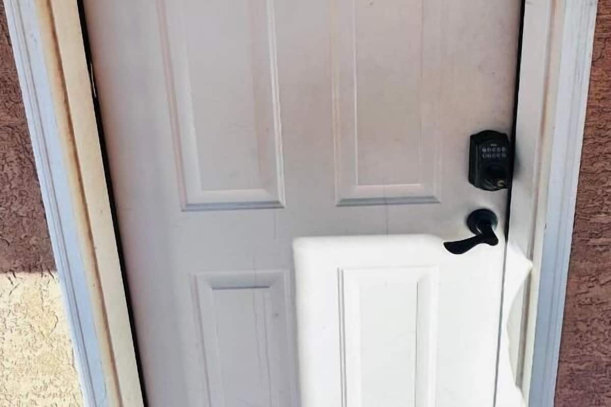 Una puerta blanca con una placa numérica pequeña y oscura en la parte superior y un timbre a la derecha.