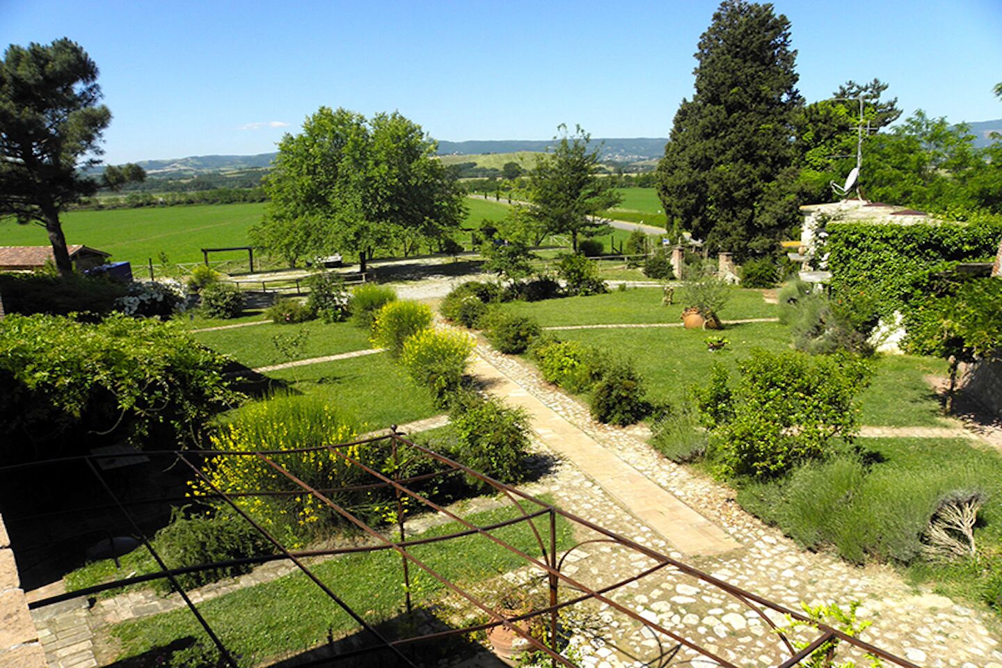 A garden with a stone pathway, various plants, and a view of the countryside.