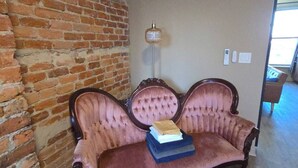 Ett rum med en tegelvägg, en soffa i vintage-stil med en bok på, en golvlampa och en mönstrad matta.