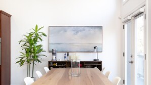 Un comedor con una mesa de madera, dos sillas, una lámpara de araña, una planta en maceta y un cuadro en la pared.